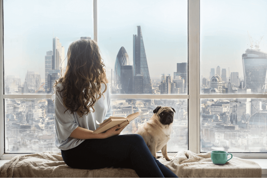 Woman sitting next to the window reading a book with her dog