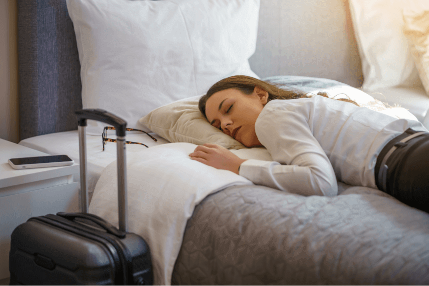 Woman lying asleep on a bed with a travel suitcase next to the bed